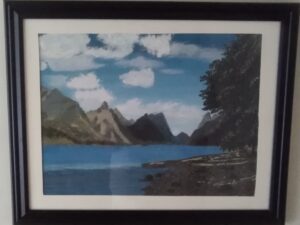 A framed painting of a lake with mountains in the background.