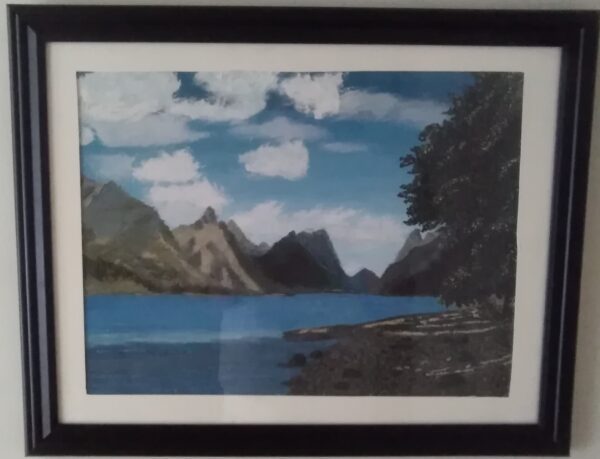 A framed painting of a lake with mountains in the background.