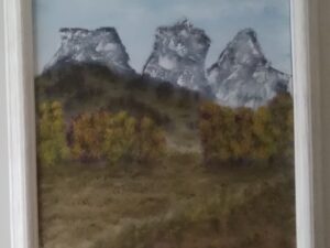 A painting of three mountains in a white frame.