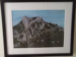 A framed painting of a mountain on a wall.