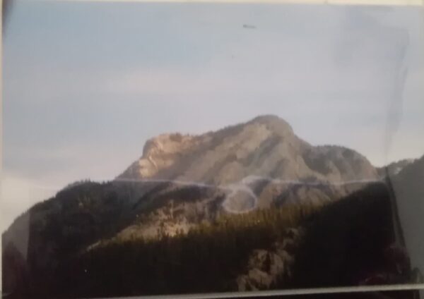 A photo of a mountain with a plane flying over it.